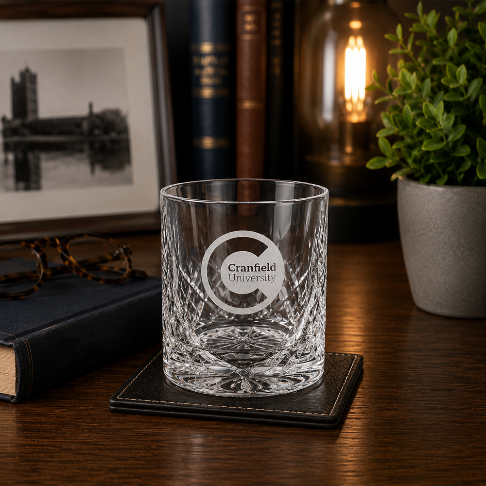 Clear glass with Cranfield University logo on a wooden surface with books and a plant in the background