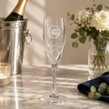 Champagne flute with branding on a marble surface with flowers and a bottle in the background