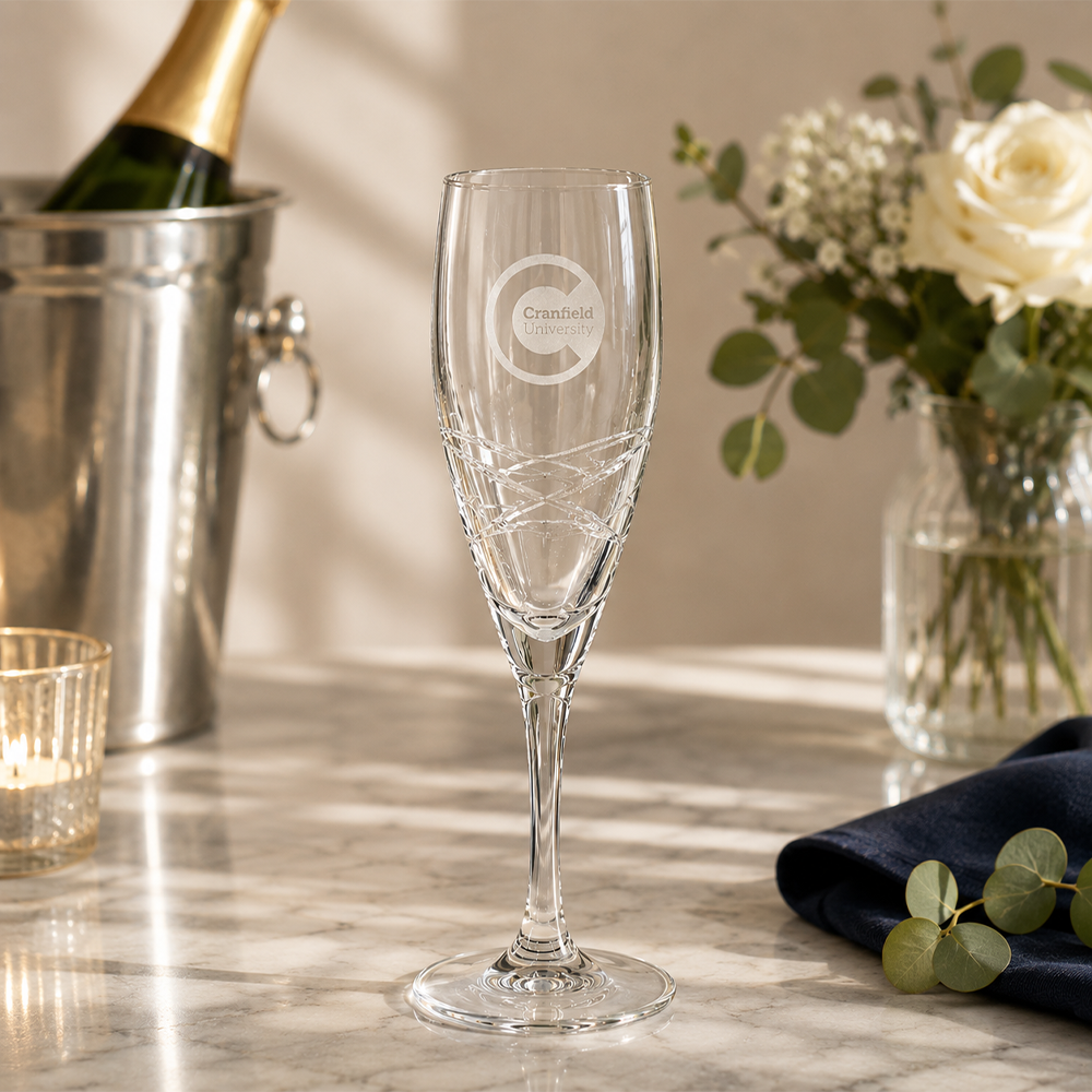 Champagne flute with branding on a marble surface with flowers and a bottle in the background