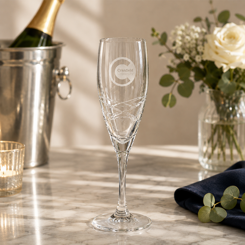 Champagne flute with branding on a marble surface with flowers and a bottle in the background
