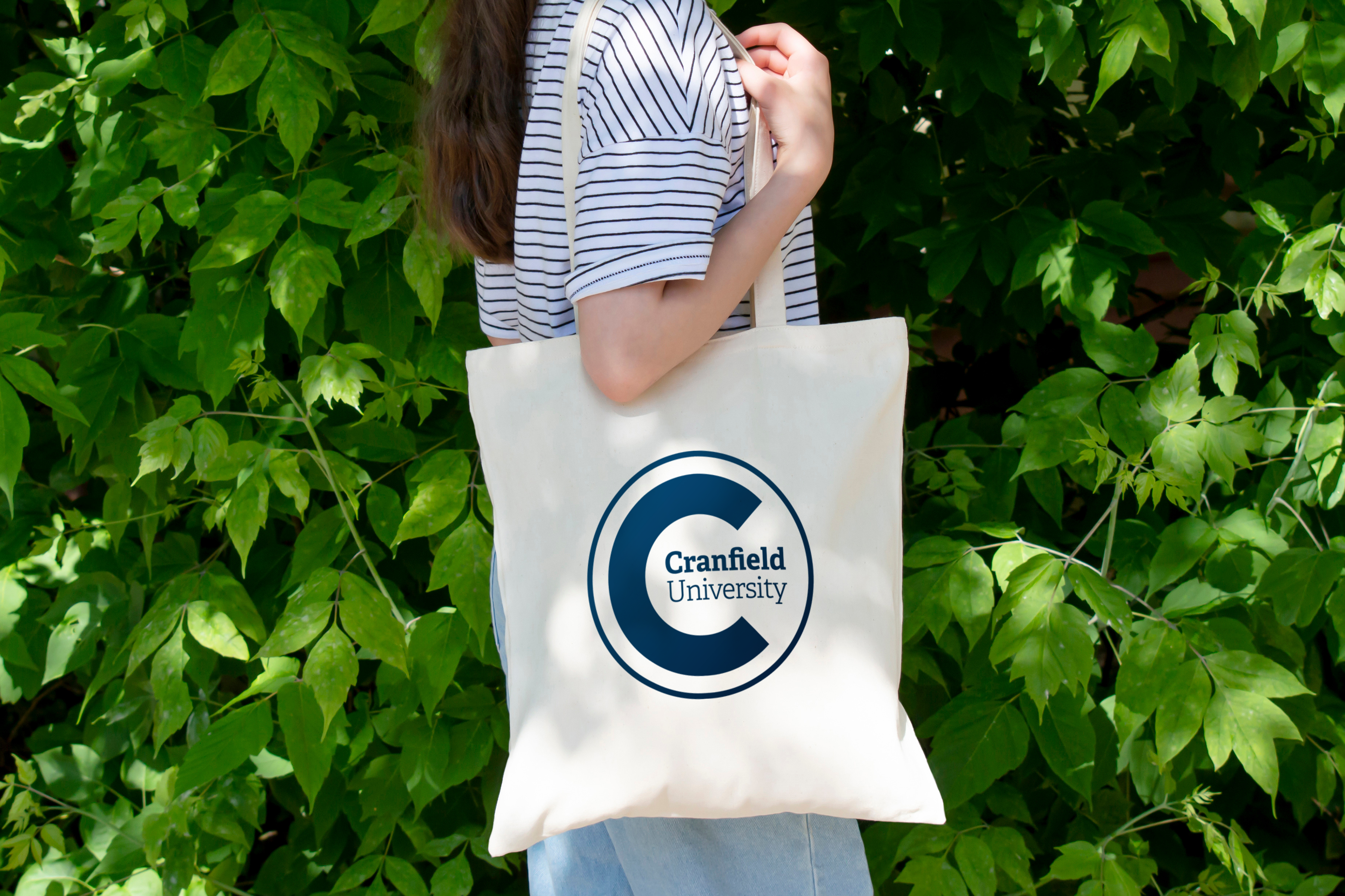 Person holding a tote bag with Granfield University logo against a green leafy background