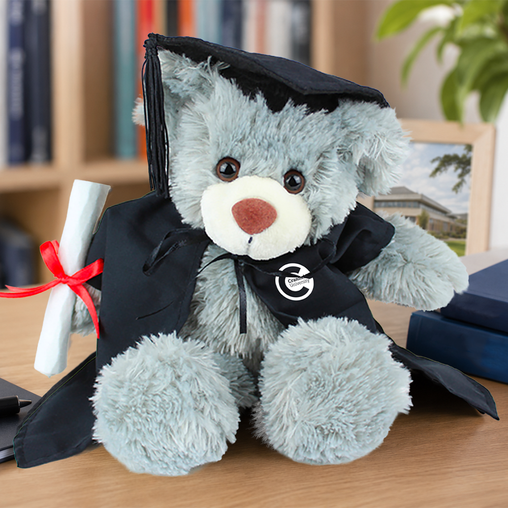Graduation-themed teddy bear with a cap, gown, and diploma on a wooden surface.